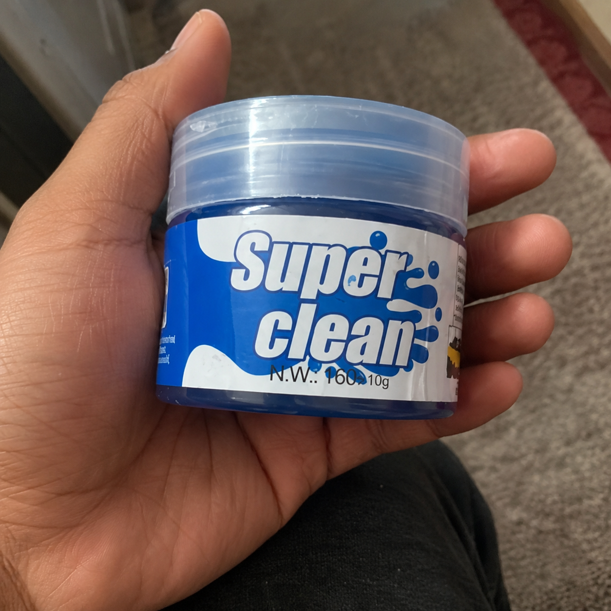 Hand holding a small container labeled 'Super Clean' against a neutral background